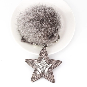 Détail du porte-clés pompon gris et étoile en strass sur une assiette en céramique blanche