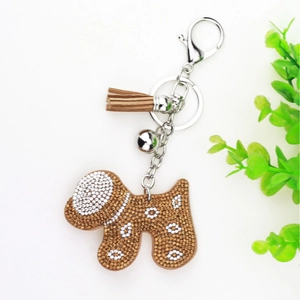 Detail of a brown rhinestone dog keychain with silver bell and leather tassel charm