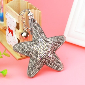 Star-shaped crystal keychain with grey tassel and small bell on a pink background