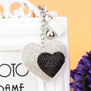 Dettaglio di un portachiavi a forma di cuore con strass bicolore, nappe bianche e campanellino