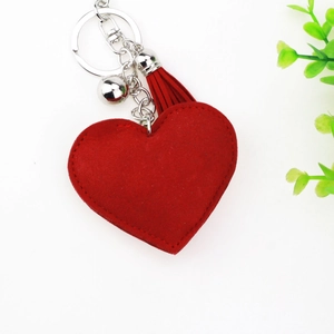 Détail macro du porte-clés cœur en daim rouge avec pompon en cuir et petite cloche