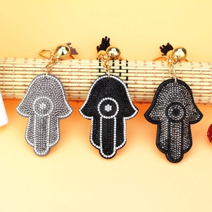 Three Hamsa hand keychains with sparkling rhinestones and black tassels on bamboo