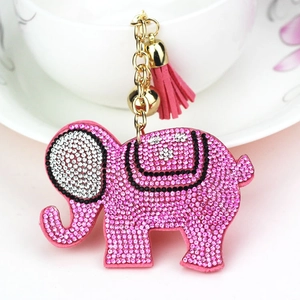 Pink rhinestone elephant keychain with gold bell and soft tassel on a ceramic cup