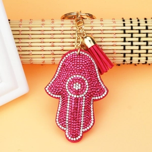 Detailed view of pink Hamsa hand charm with rhinestones, golden ring, and red tassel