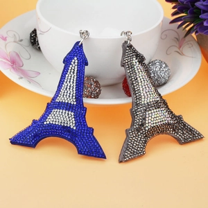 Detail of Eiffel Tower rhinestone earrings in blue and grey hanging on a ceramic cup