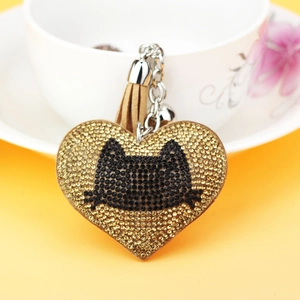 Detail of heart keychain with cat silhouette and light brown leather tassel on yellow backdrop