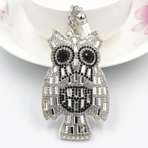 Detail of owl keychain with white rhinestones, silver chain and leather tassel on a cup