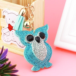 Detailed close-up of a blue owl keychain with rhinestones, leather tassel, and bell