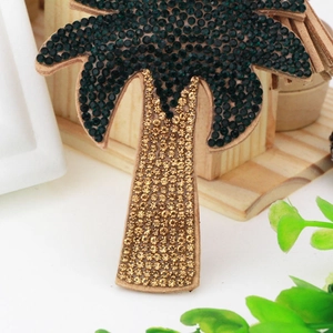 Detailed macro view of a tropical palm tree brooch with emerald and gold rhinestones