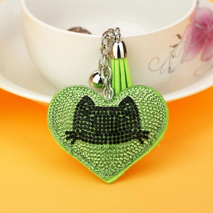 Detailed view of green rhinestone heart keychain with a cat face, tassel and silver bell