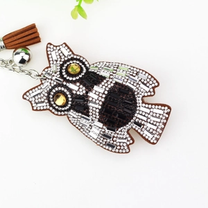 Detail view of crystal owl keychain with brown leather backing and tassel charm