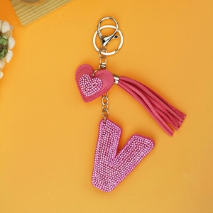 Detail of pink crystal letter V keychain with heart charm and tassel on yellow background