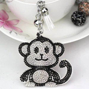 Close-up of rhinestone monkey keychain with white tassel and silver bell detail on a plate
