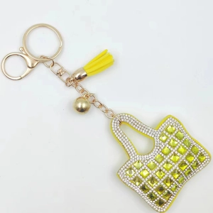 Miniature yellow bag keychain with green square crystals and tassel on a white background