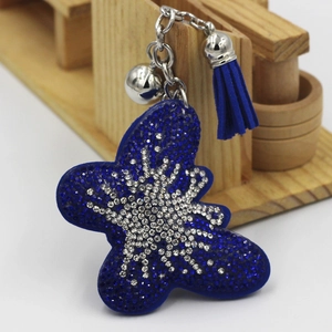Détail d'un porte-clés papillon avec strass bleus, petite clochette et pompon en daim
