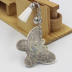 Détail du porte-clés papillon avec strass colorés, clochette argentée et gland blanc