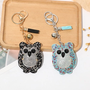 Détail de porte-clés hibou avec strass, pompons et clochettes sur un plateau en bois