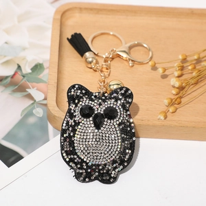 Détail d'un porte-clés chouette en strass noirs et blancs avec pompon et clochette dorée
