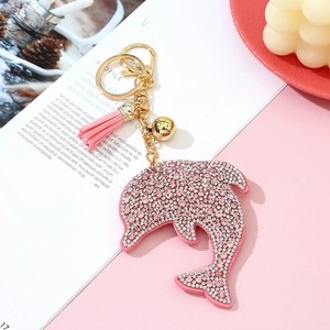 Pink crystal rhinestone dolphin keychain with tassel and gold bell on a magazine