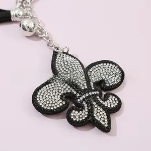 Détail d'un porte-clés fleur de lys avec strass, chaîne argentée et pompon noir élégant