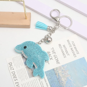 Porte-clés dauphin en strass bleu avec pompon en cuir et fermoir argenté sur fond blanc