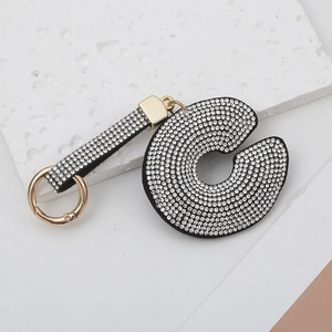 Porte-clés avec lettre en strass étincelant et anneau doré sur un fond de pierre blanche