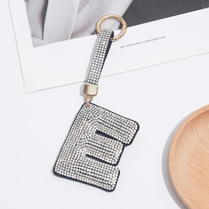 Close-up of letter E keychain with black base and sparkling rhinestones on white surface