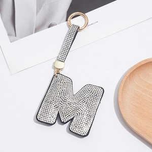 Detail view of crystal rhinestone letter M keychain with gold hardware on white background