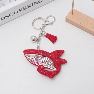 Detailed macro view of a red rhinestone shark keychain with a silver bell and leather tassel