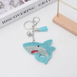 Sparkling blue rhinestone shark keychain with fringe and silver lobster clasp on white desk