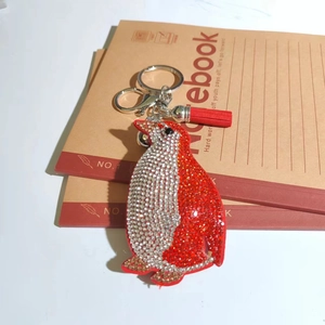 Close-up of a crystal penguin keychain with red rhinestones and a silk tassel on notebooks