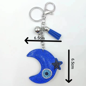 Detailed view of blue moon keychain with rhinestones, evil eye motif and blue fringe tassel