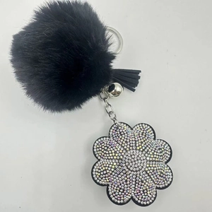 Close-up of a black faux fur pompom keychain with a rhinestone flower charm and tassel