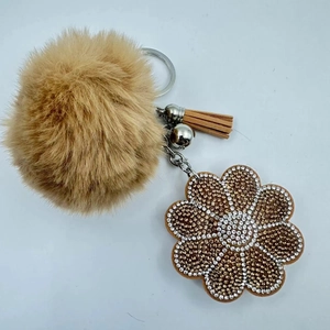 Detailed view of plush keychain with brown faux fur ball, tassel and rhinestone flower charm