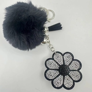 Close-up of black faux fur pompom keychain with rhinestone flower and silver bell detail