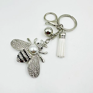 Close-up of silver bee charm featuring rhinestones, white pearl and leather tassel