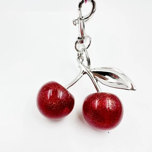 Porte-clés cerise rouge pailleté avec feuilles en métal argenté sur un fond blanc neutre