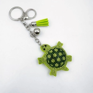 Détail d'un porte-clés tortue en strass avec pompon vert et fermoir argenté brillant