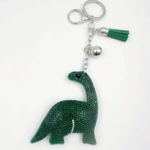 Green crystal dinosaur keychain with tassel and bell on a minimalist white background