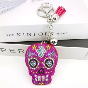 Sparkly rhinestone skull keychain with pink leather tassel and bell on white books