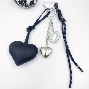 Detail of black leather heart keychain with silver diamond letter O and woven rope strap