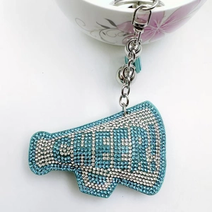 Detail of megaphone keychain with blue rhinestones, silver chain, bell and fringe charm