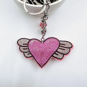 Sparkling pink rhinestone heart keychain with wings and tassel on a white surface