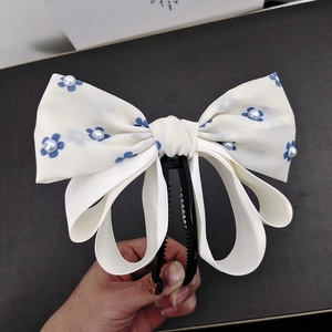 Detail of cream fabric bow hair clip with blue floral pattern and faux pearl accents