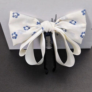 Detail of elegant bow banana clip with blue floral pattern and white pearl accents