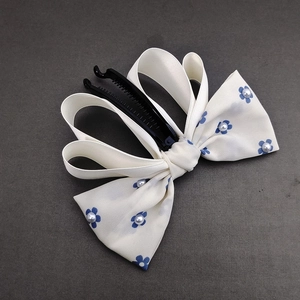 Close-up of cream bow banana hair clip with blue floral pattern and pearl accents