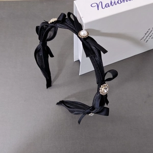 Detailed macro view of black satin bow headband featuring elegant pearls and sparkling rhinestones