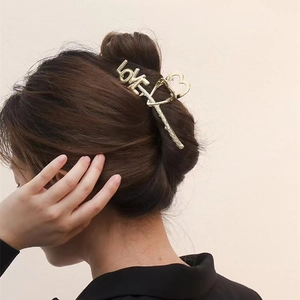 Detail view of a gold metal hair claw clip with LOVE letters and heart cutouts on hair