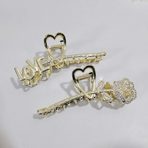 Detailed close-up of golden metal hair claws with rose rhinestones and LOVE lettering