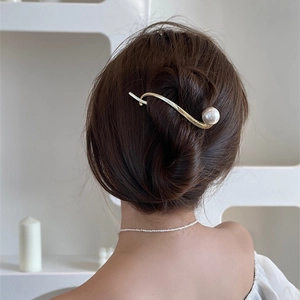 Spilla per capelli dorata a S con grande perla bianca su un’acconciatura a chignon